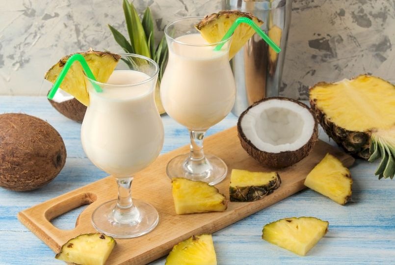 dwa drinki na bazie kokosa podane na deseczce ozdobione kokosem i ananasem